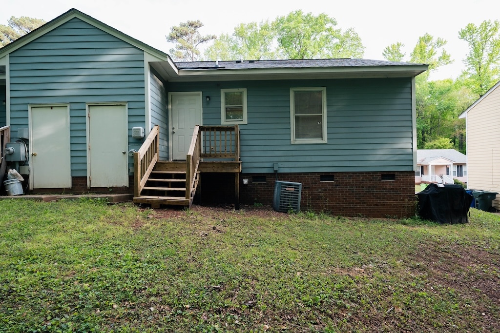 Rear view of a blue single-story house with a small wooden staircase, two doors, several windows, and an air conditioning unit on a grassy yard.